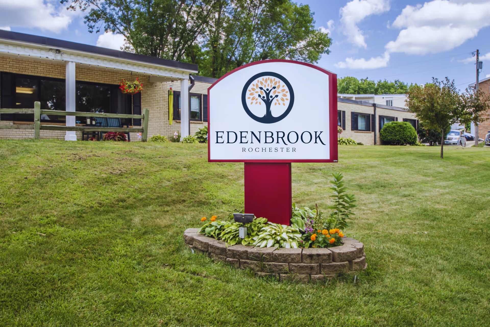 A landscaped sign reading "Edenbrook Rochester" on a lawn in front of a single-story brick senior living building.