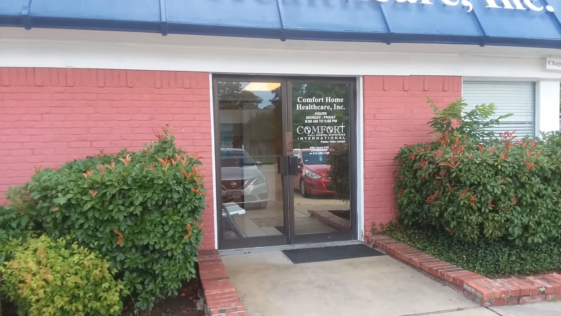 Exterior view of Comfort Home Health Care entrance with glass door and surrounding shrubs