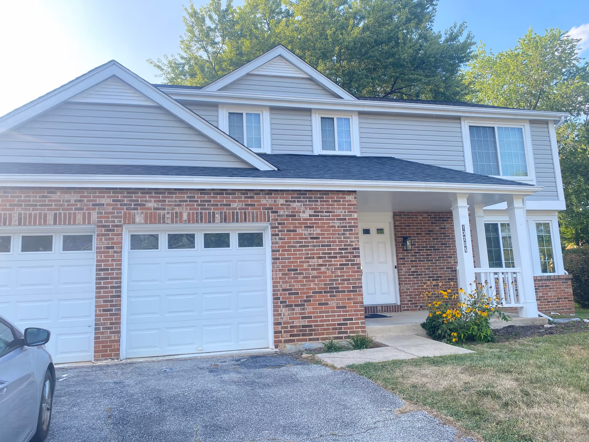 Two-story building exterior with brick lower level, gray siding, white garage doors, and a front porch.