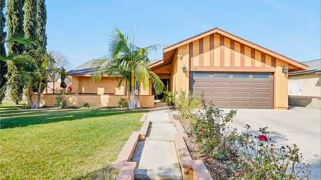 Front view of a single-story assisted living facility with a driveway and palm trees.