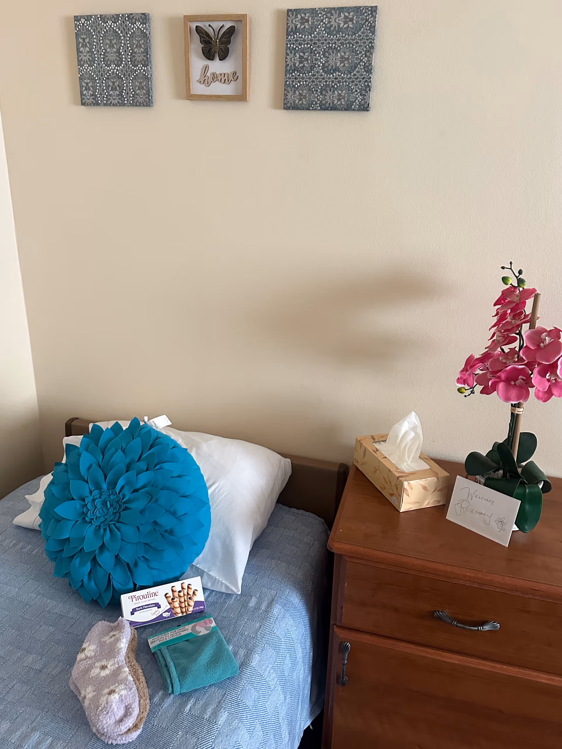 A bedroom in a senior facility featuring a blue bedspread, nightstand, and orchid.