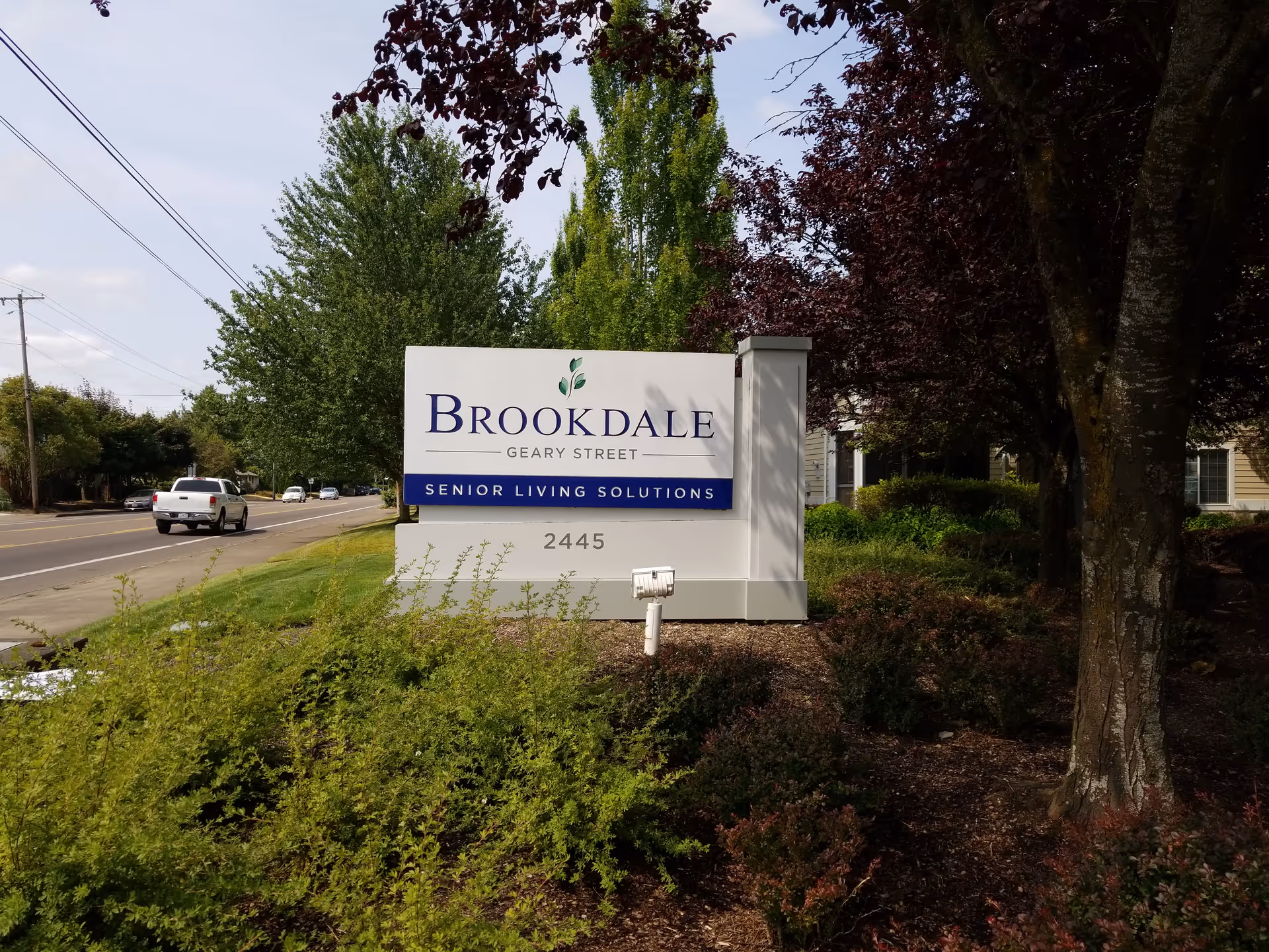 Brookdale Geary Street sign sits beside trees and a roadway.