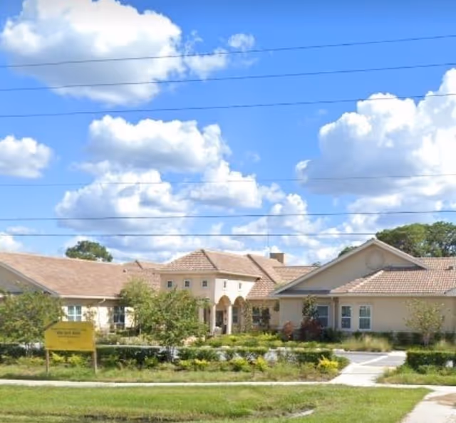 Exterior view of Liana of Sarasota senior living facility with landscaped front and blue sky.