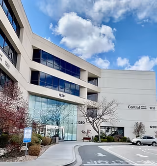Contemporary medical office building exterior with glass entrance and parking area beneath a blue sky.