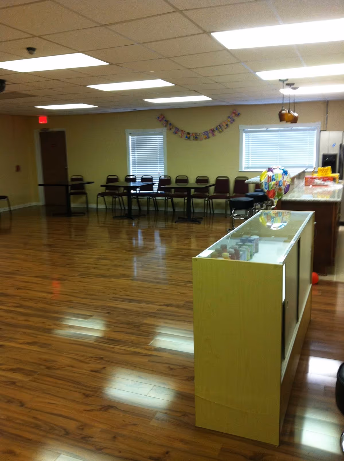 A spacious indoor common area with wooden floors, row of chairs, and a glass display case.