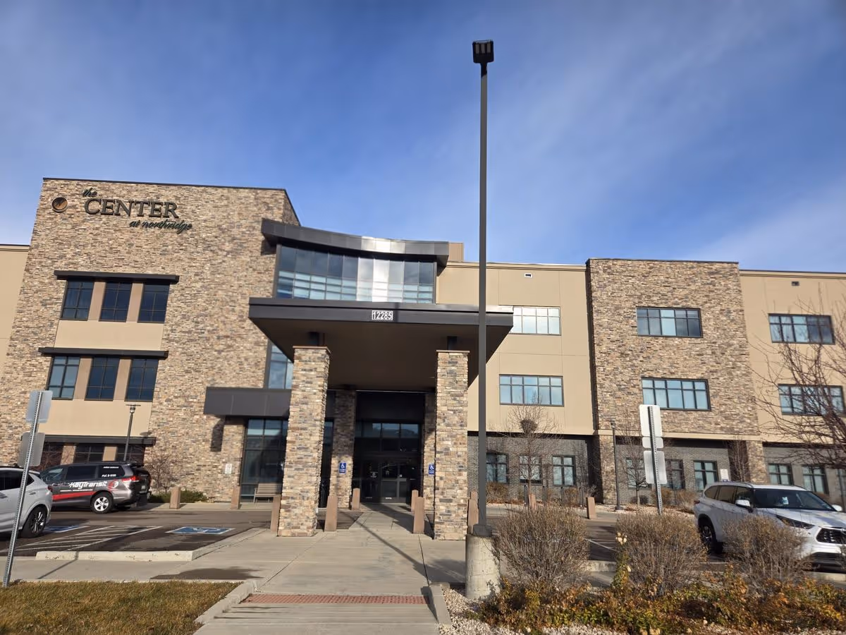 Front exterior of The Center at Northridge, a three-story stone-faced building with a covered main entrance and parked cars.