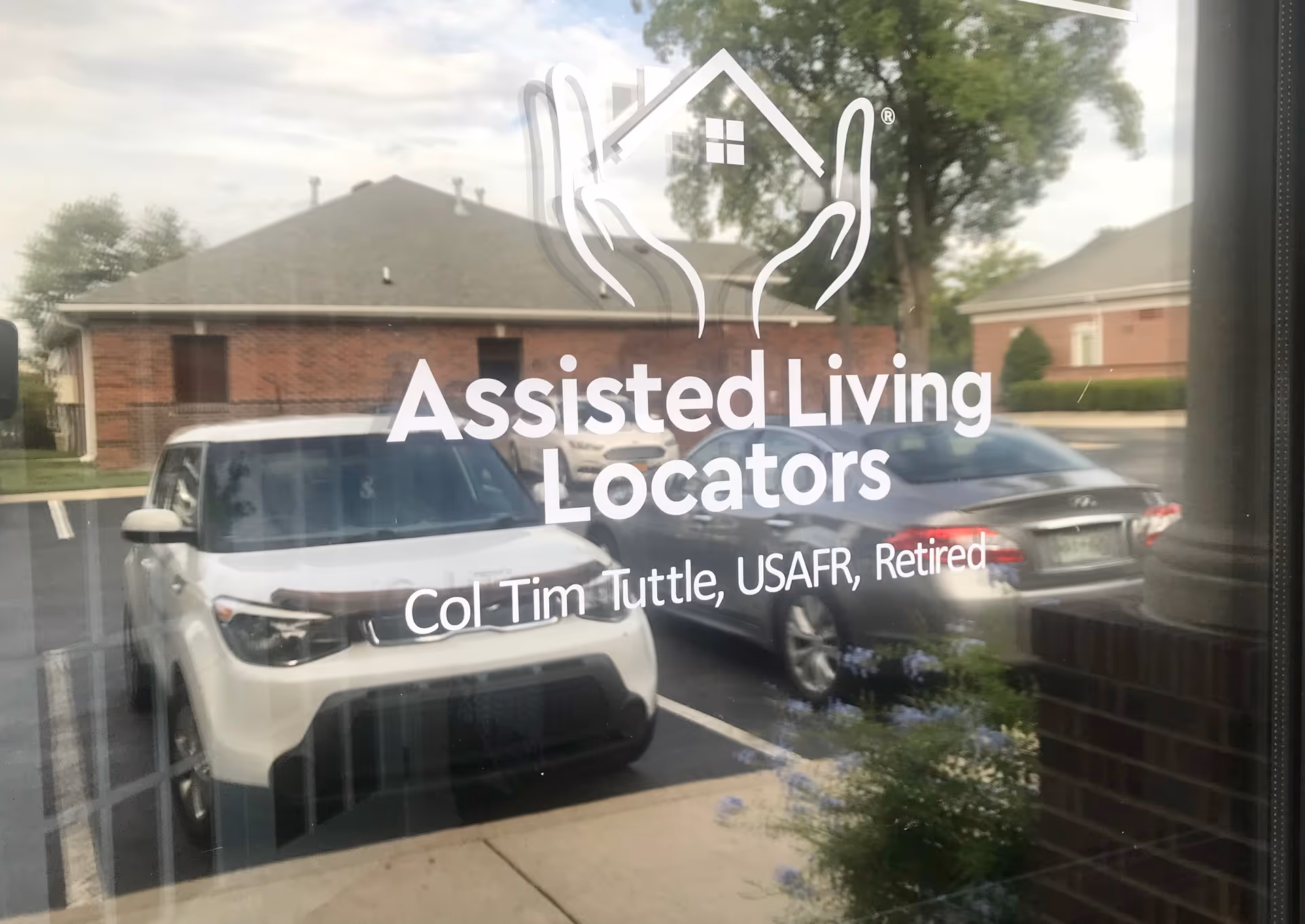 Glass window displays 'Assisted Living Locators' logo and text; reflections show parked cars outside.