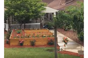 Raised wooden planters with flowers in a front yard near a brick building.