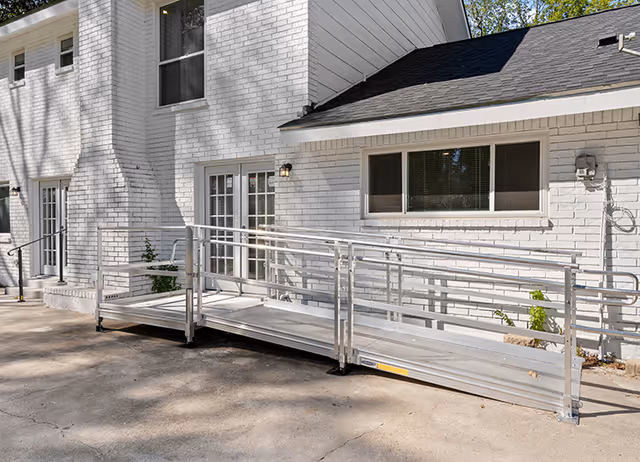 Exterior of a white brick senior living building featuring a metal wheelchair ramp and doorway.
