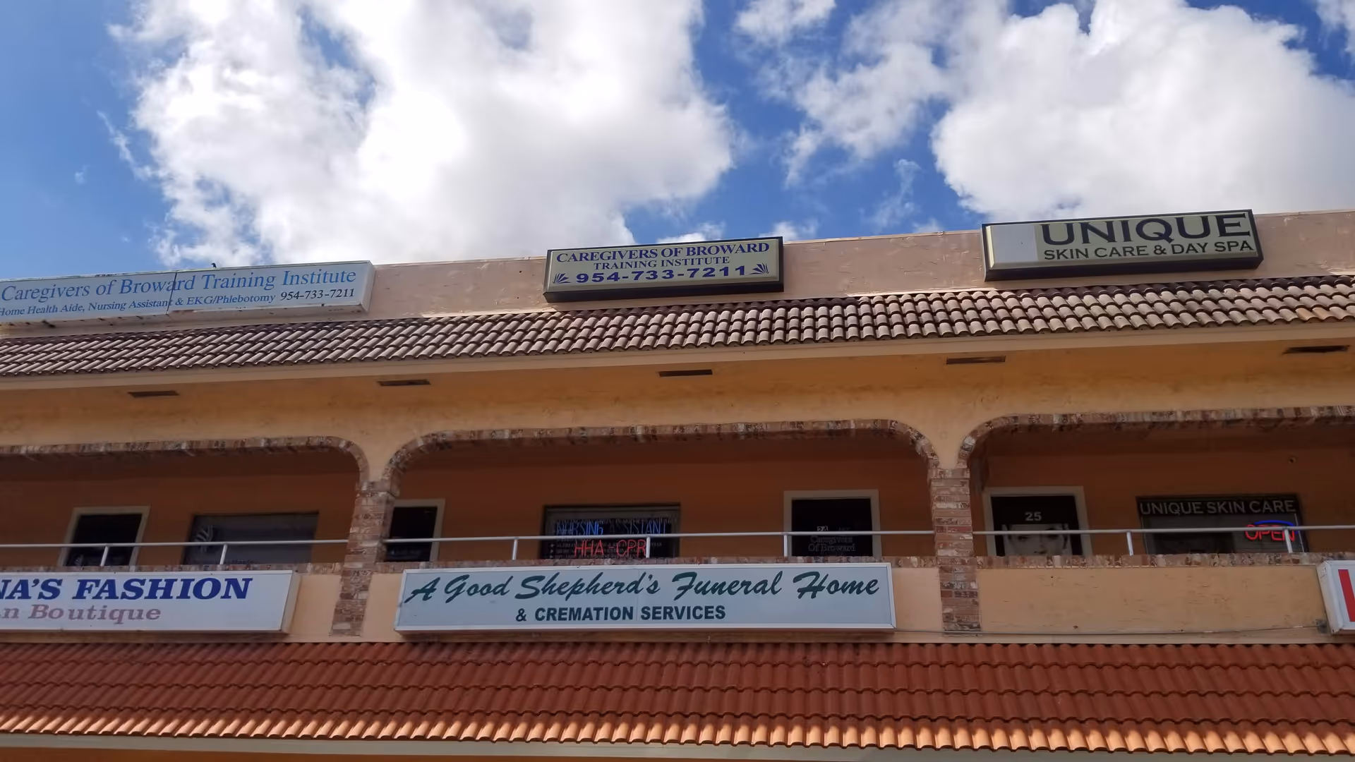 Beige building exterior with signs including Caregivers of Broward under a tiled roof.