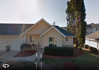 Front facade of a single-story senior care facility with trimmed bushes and driveway.
