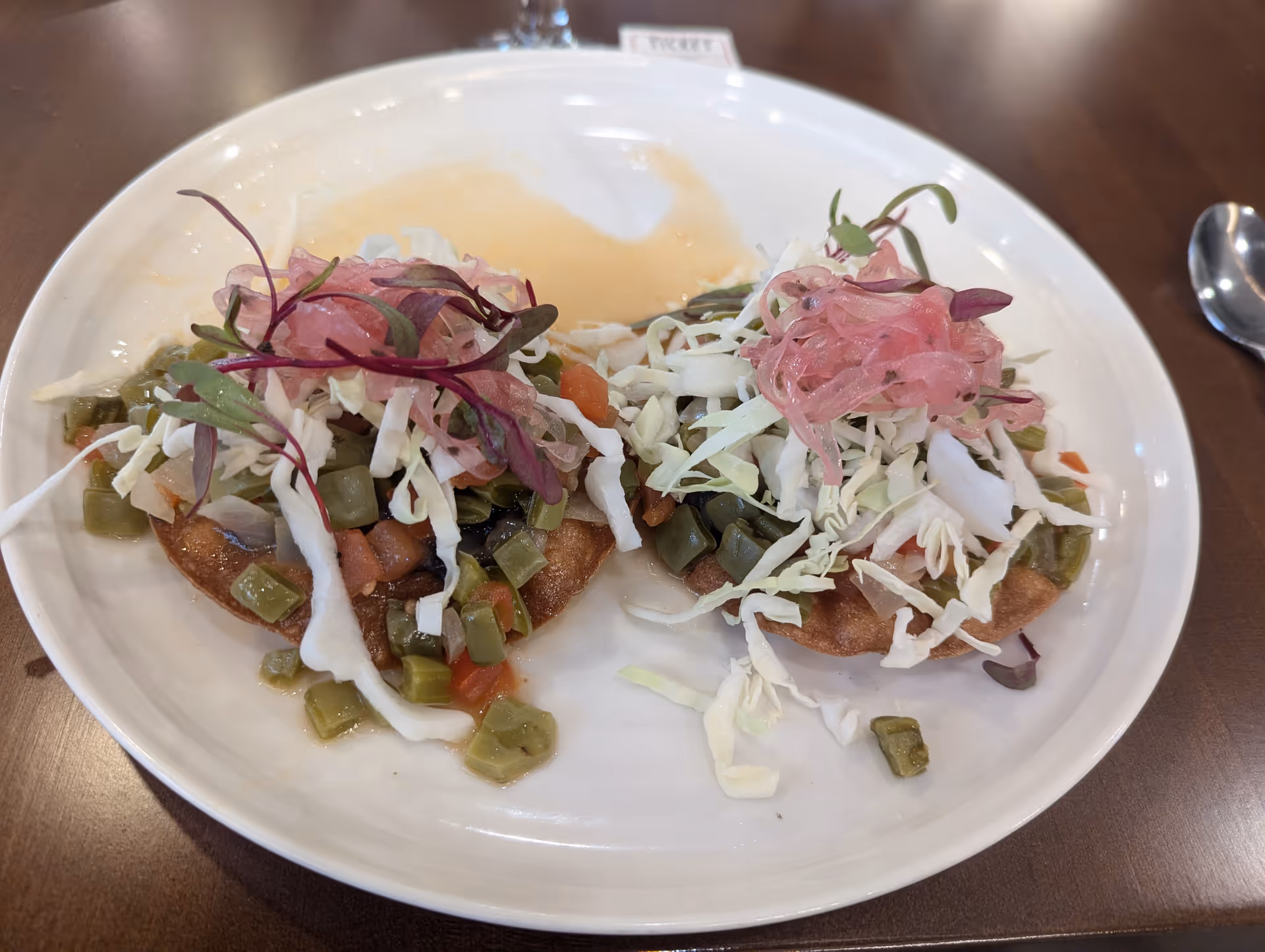 Two veggie-topped tostadas with shredded cabbage and pickled onions on a white plate.