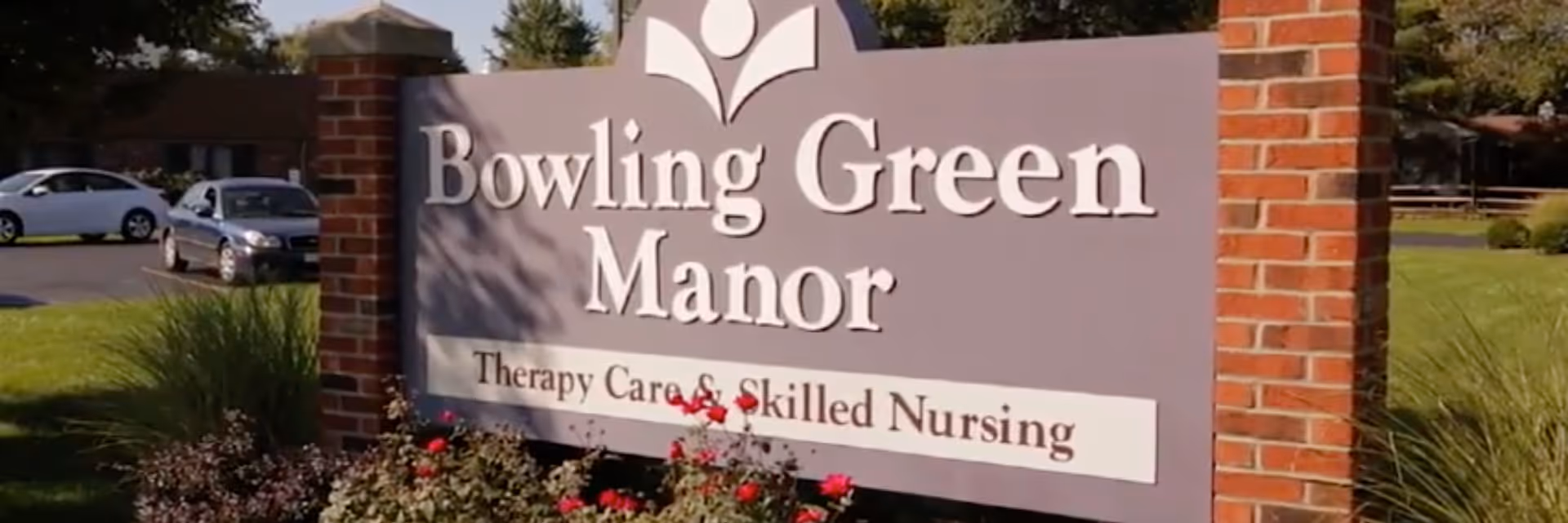 Bowling Green Manor sign on brick entrance with parked cars nearby