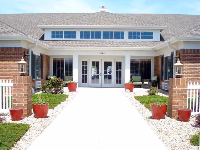 Front exterior of Country Place Senior Living Marysville with brick facade, glass doors, and red planters.
