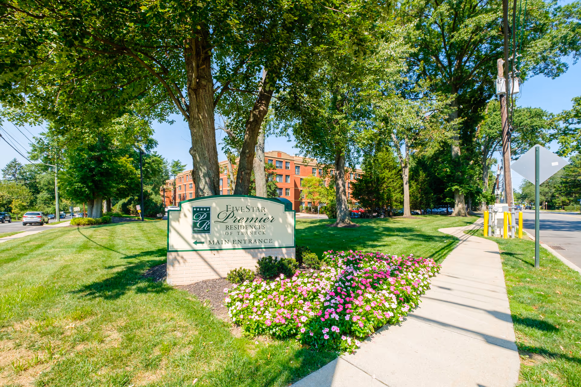 Landscaped front lawn and flowerbed with a Five Star Premier Residences of Teaneck sign in front of a brick residence and sidewalk.