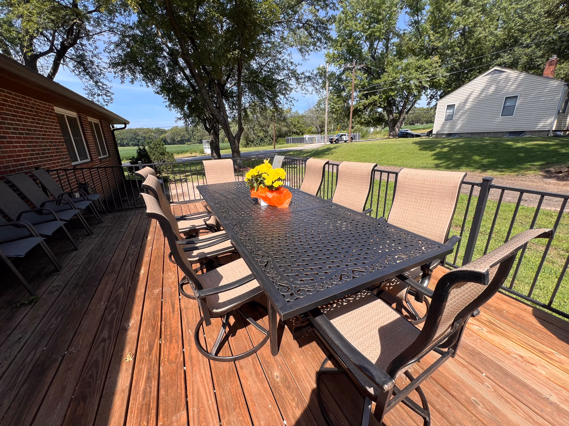 Outdoor wooden deck with a wrought-iron table, chairs, and a yellow flower centerpiece.