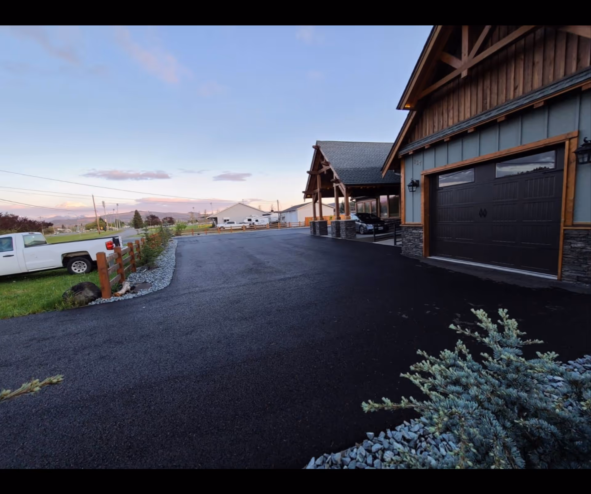 Exterior view of a rustic building with a paved driveway and a white pickup nearby.