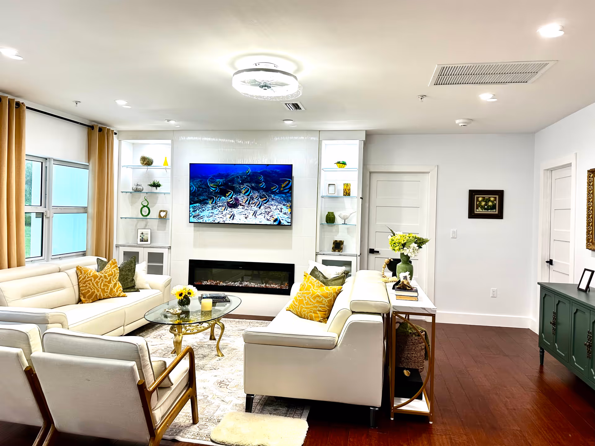 Bright, modern living room in a senior facility with white furnishings and a wall-mounted TV.