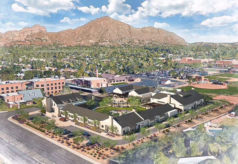 Aerial view of a senior living campus with beige buildings, parking, and mountains.