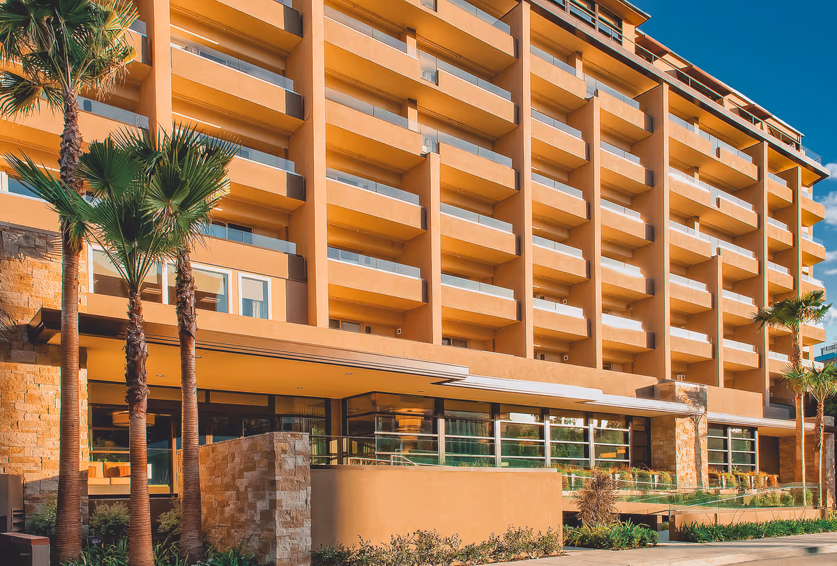 Sunlit exterior of a multi-story senior living building with balconies and palm trees.