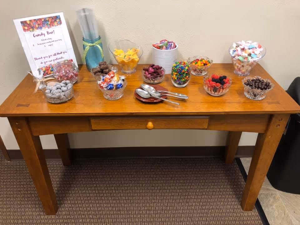 Wooden table with glass bowls of candies and toppings labeled Candy Bar.