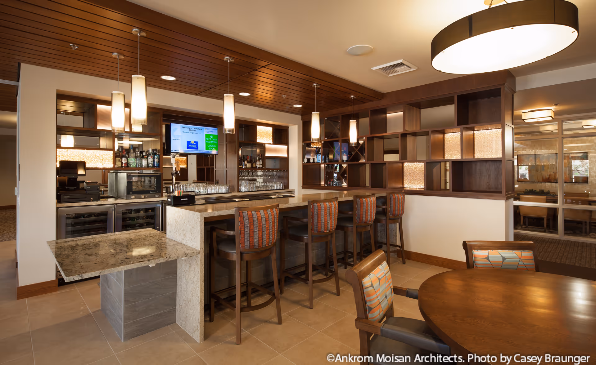 Well-lit indoor bar and dining area with a marble counter, bar stools, pendant lights, and shelving.