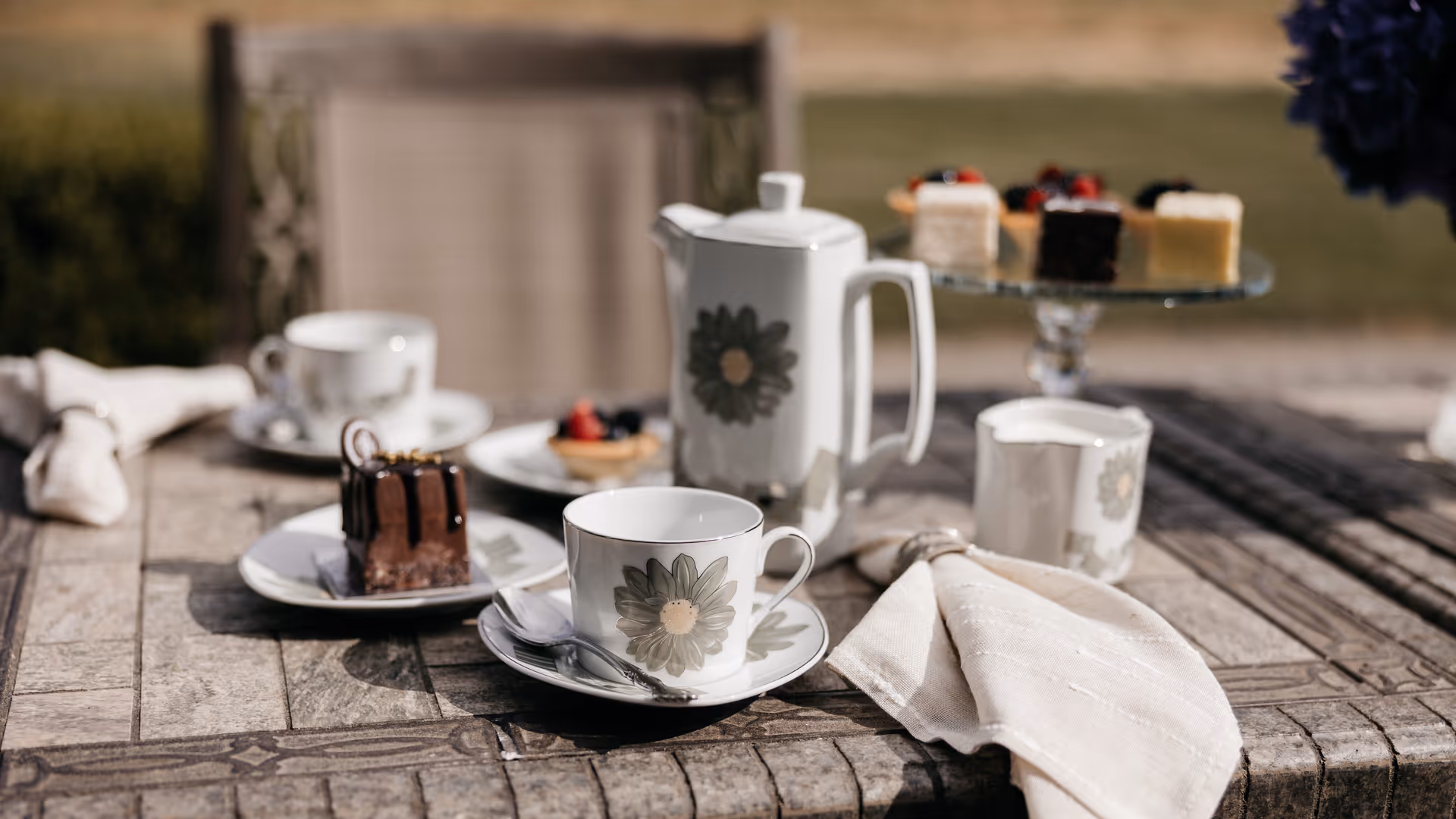 Outdoor tea setup with cups, a teapot, and desserts on a wooden table.
