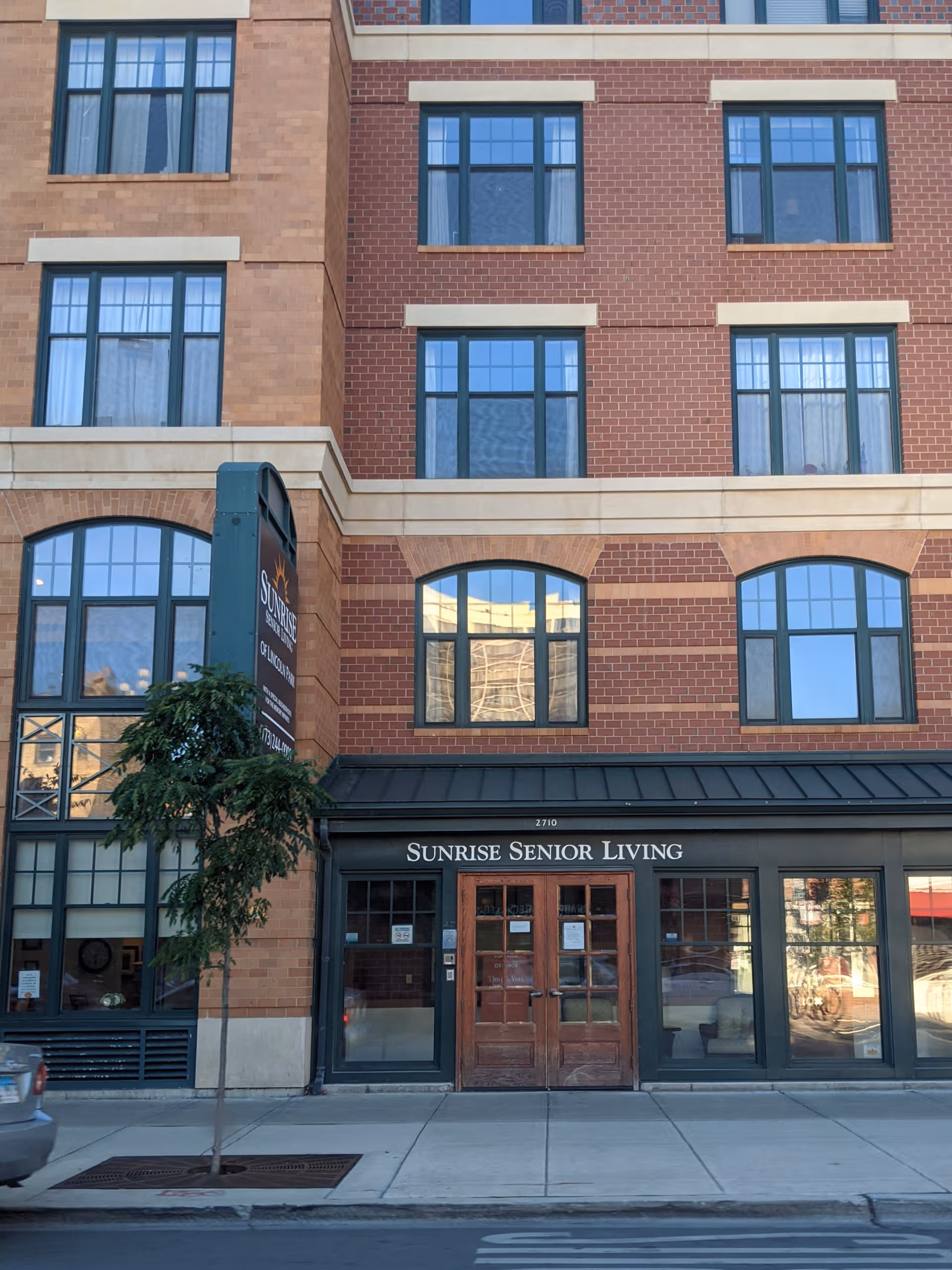 Brick building facade with Sunrise Senior Living sign and glass doors.