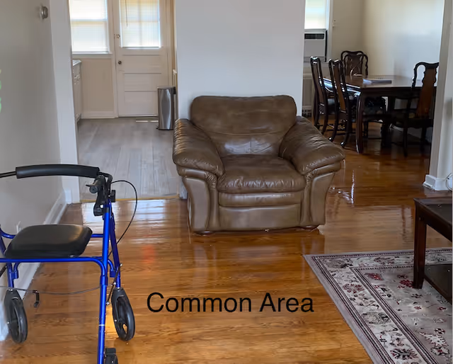 Brown leather armchair in a common area with a walker and dining room nearby.