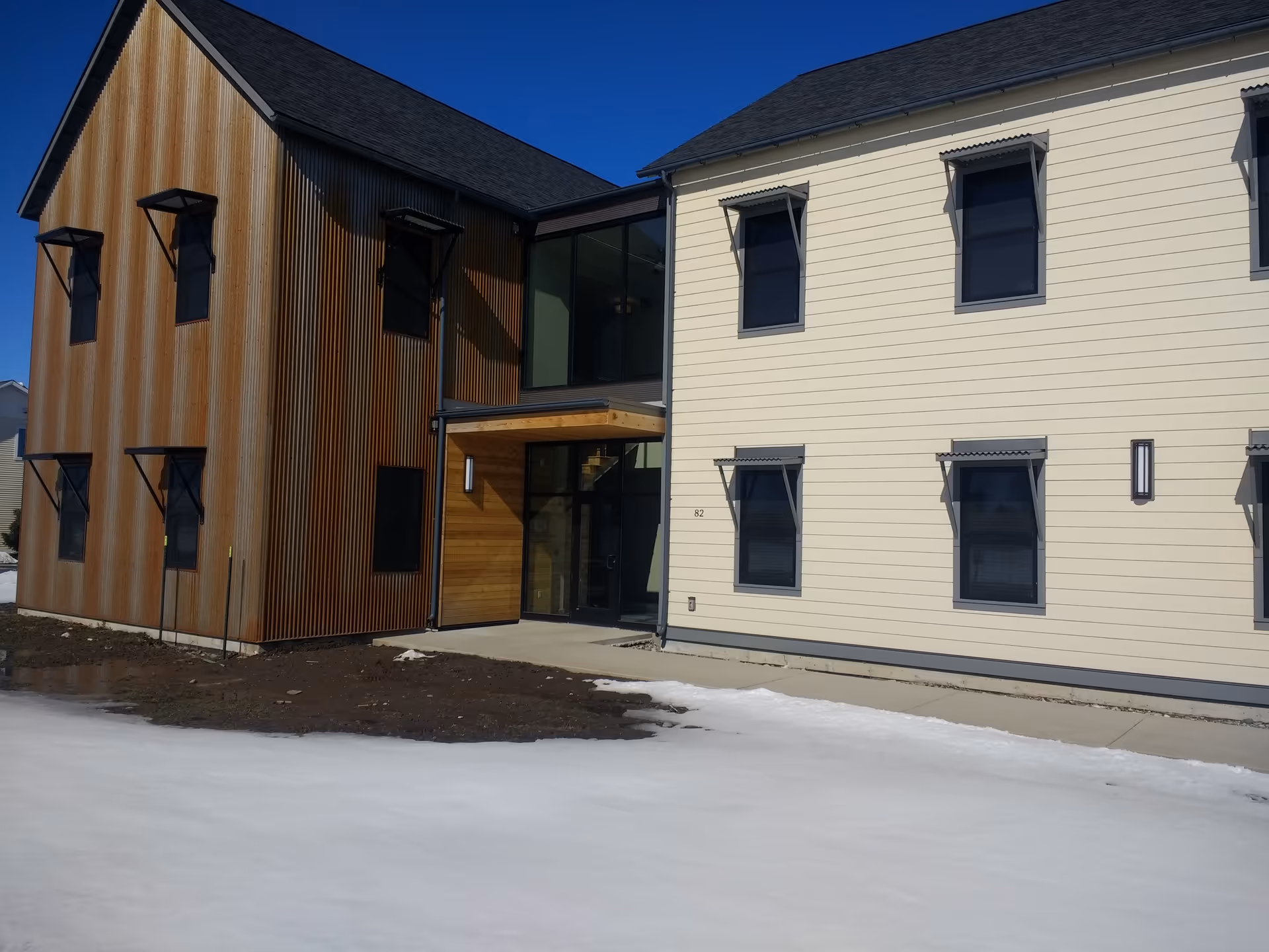 Modern two-tone building exterior with glass entry, rust-colored corrugated siding, and snow in foreground