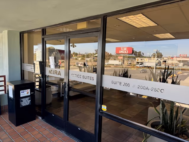Glass door entrance to an office lobby with suite signage and potted plants