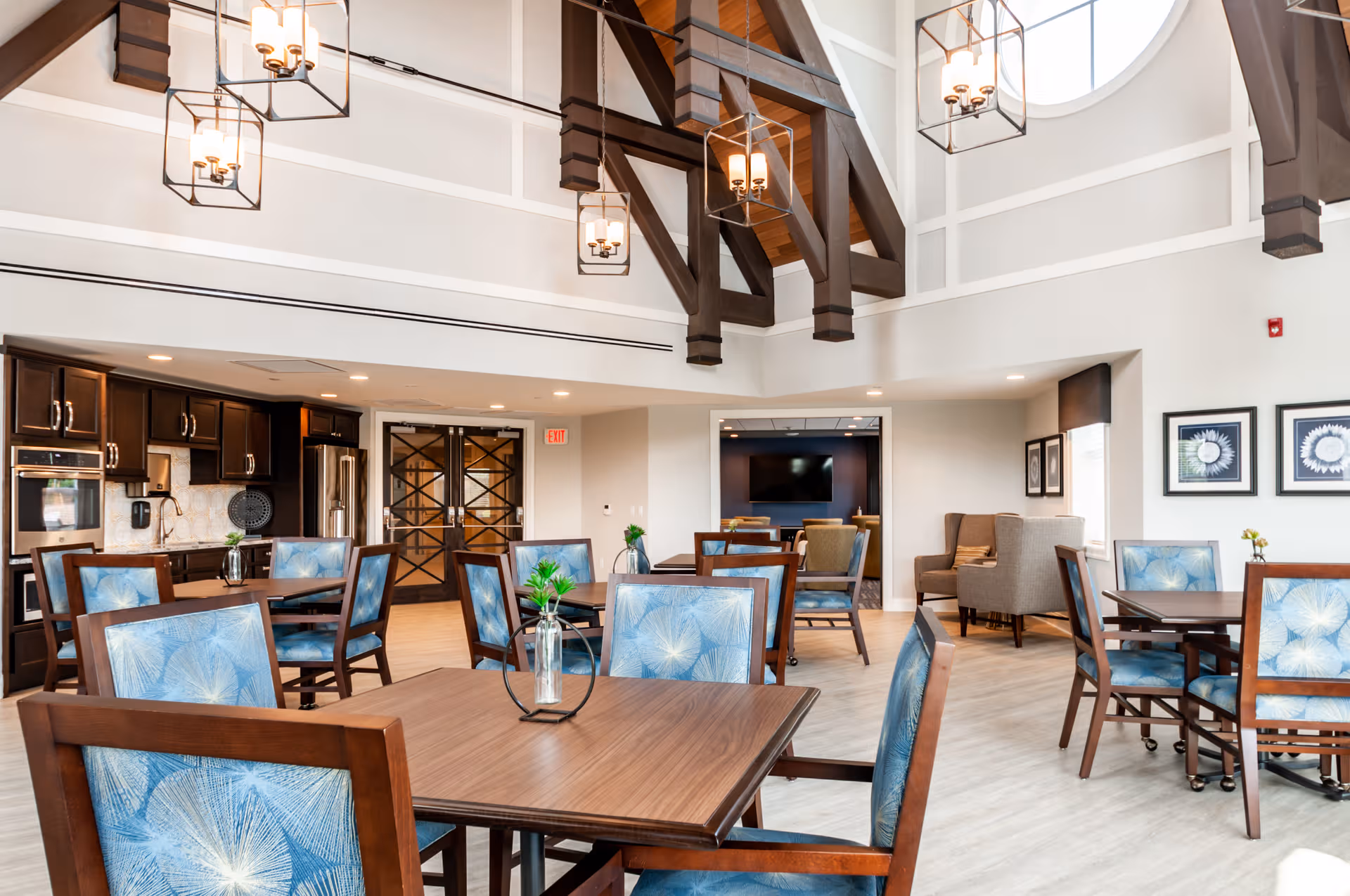 Spacious dining area with wooden tables, blue upholstered chairs, and a visible kitchen in back.
