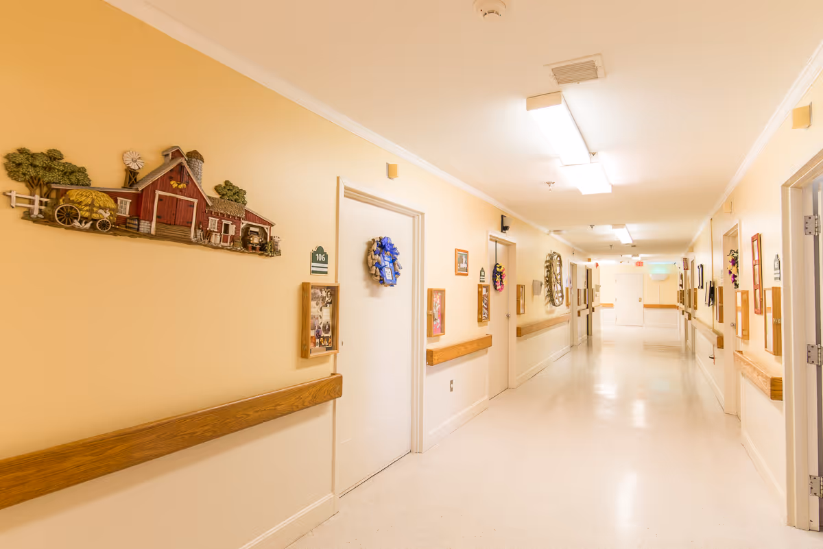 Bright, decorated hallway in a senior living facility with doors, handrails, and wall-mounted decorations.