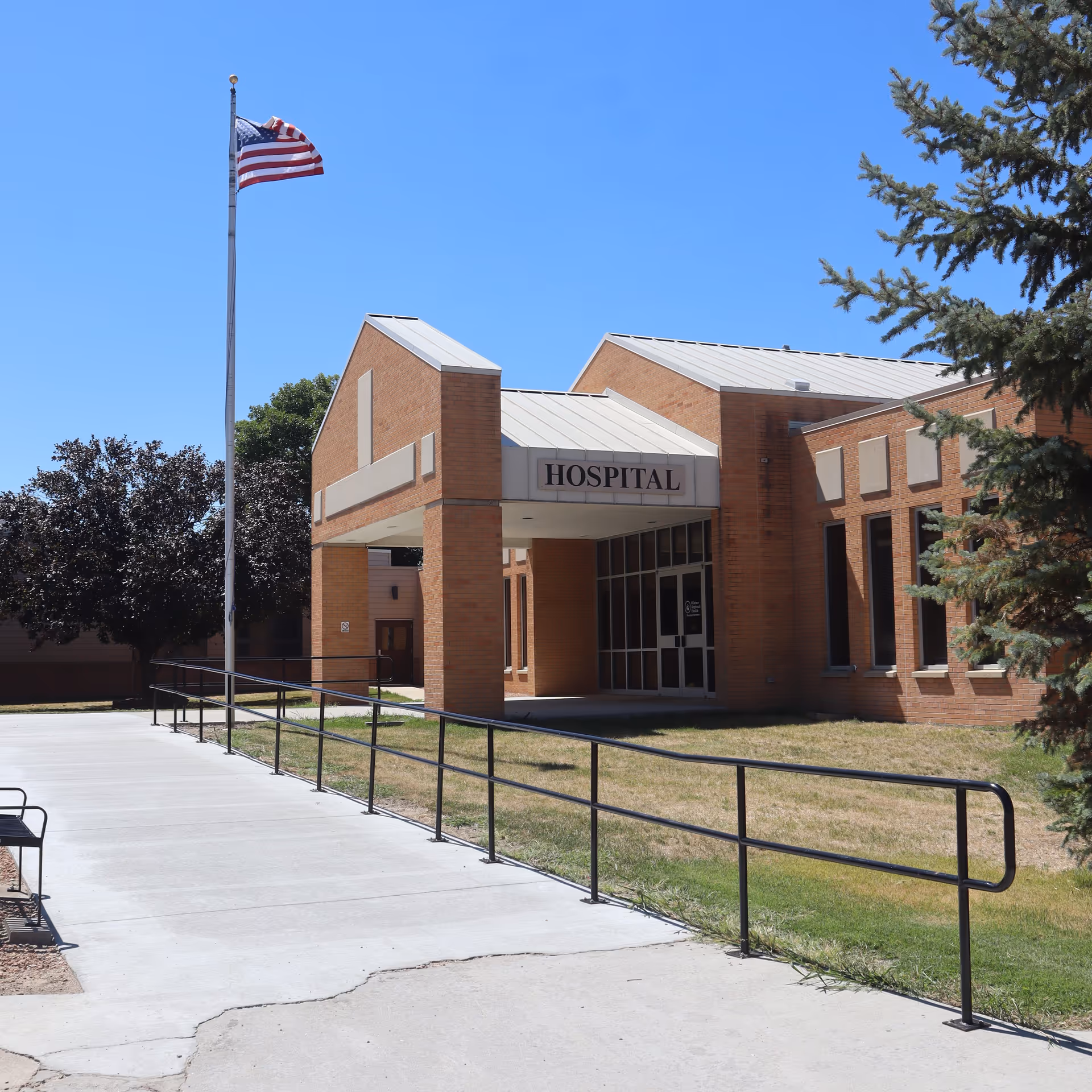 Brick hospital building with entrance, flagpole, and accessible ramp.