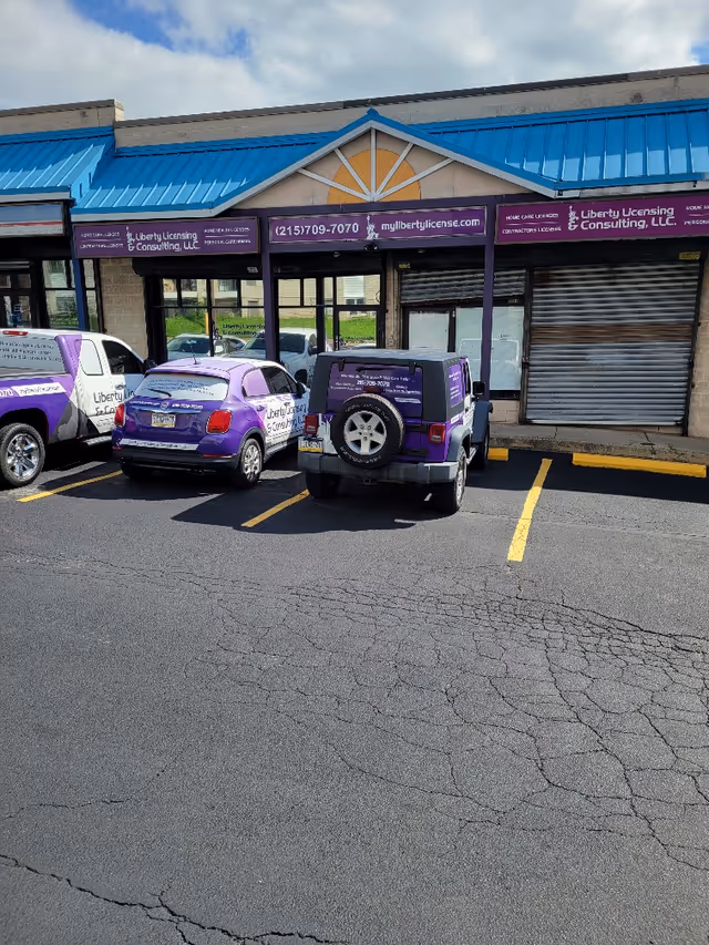 Exterior storefront of Liberty Licensing & Consulting with purple branded vehicles parked outside.
