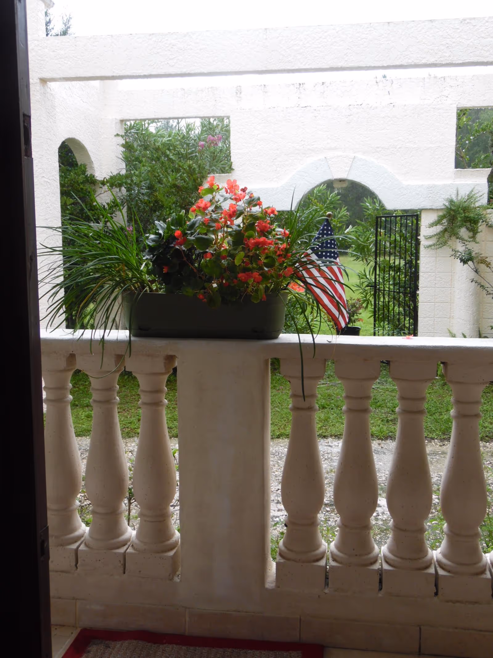Flower-filled balcony railing with a planter, greenery, and an American flag.