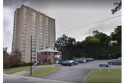 Tall senior living building with curved entry, portico, and cars parked outside.