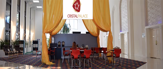 Interior hall with gold curtains, red chairs around tables, and a Cristal Palace stage backdrop.