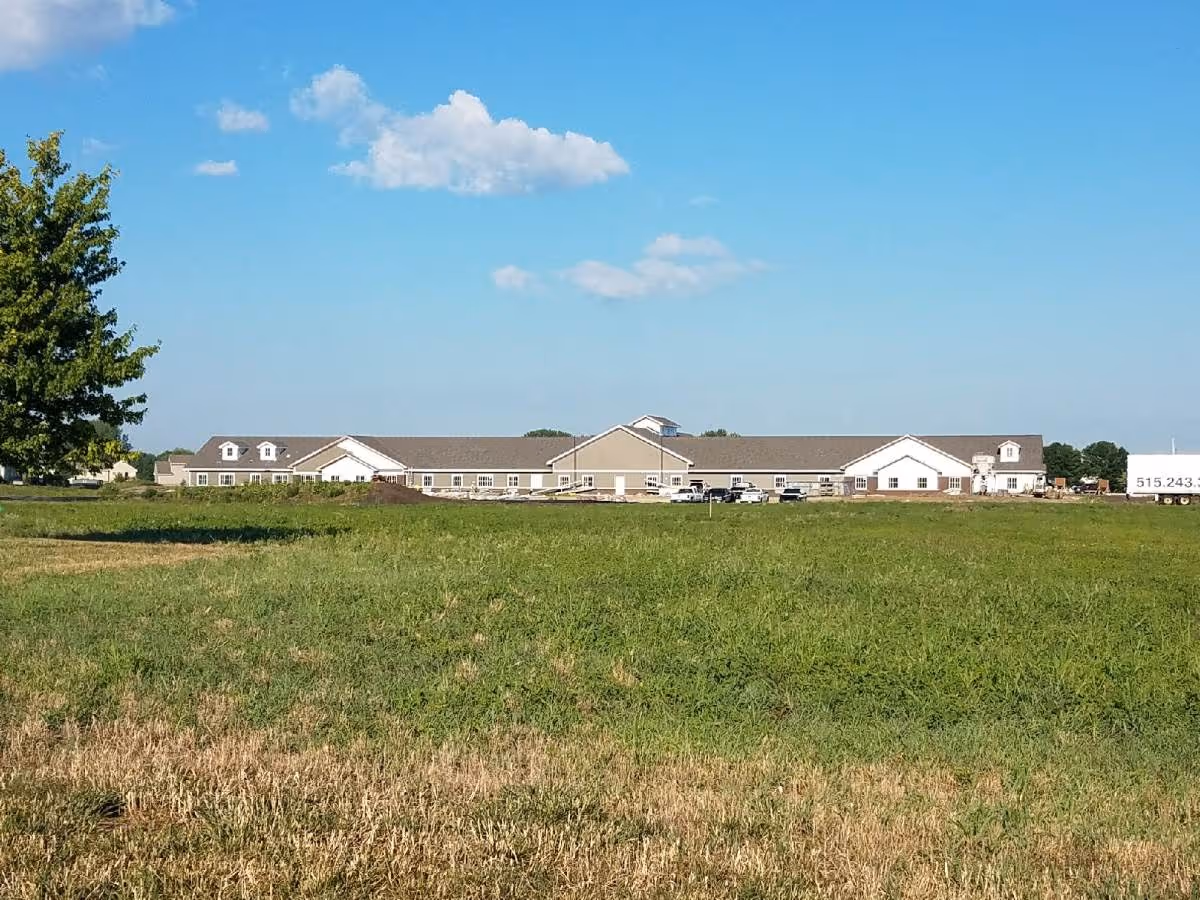 Long single-story residential building seen across a wide grassy field under a clear blue sky.