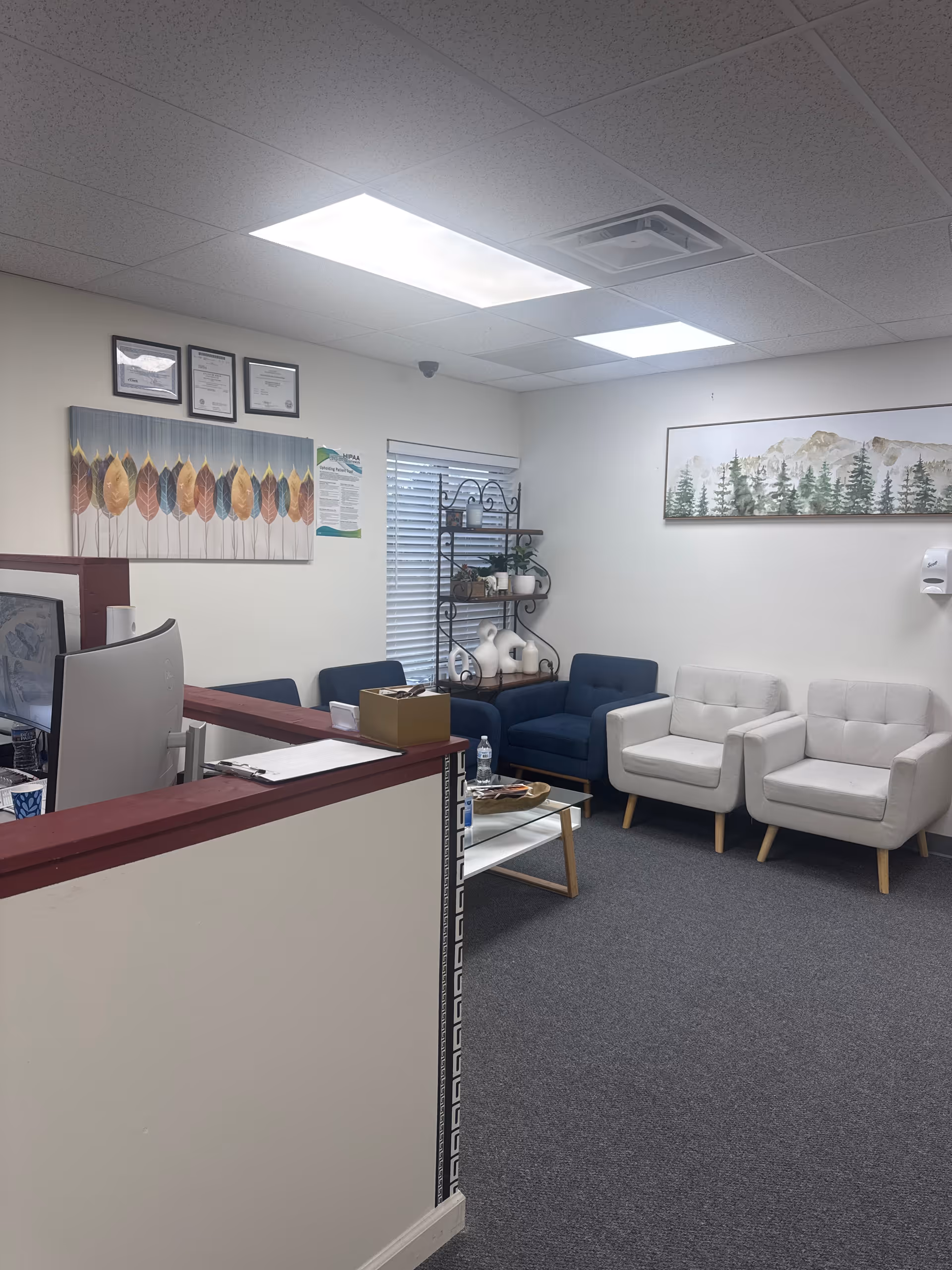 Reception lobby with a desk, blue and white chairs, wall art, and a shelving unit.
