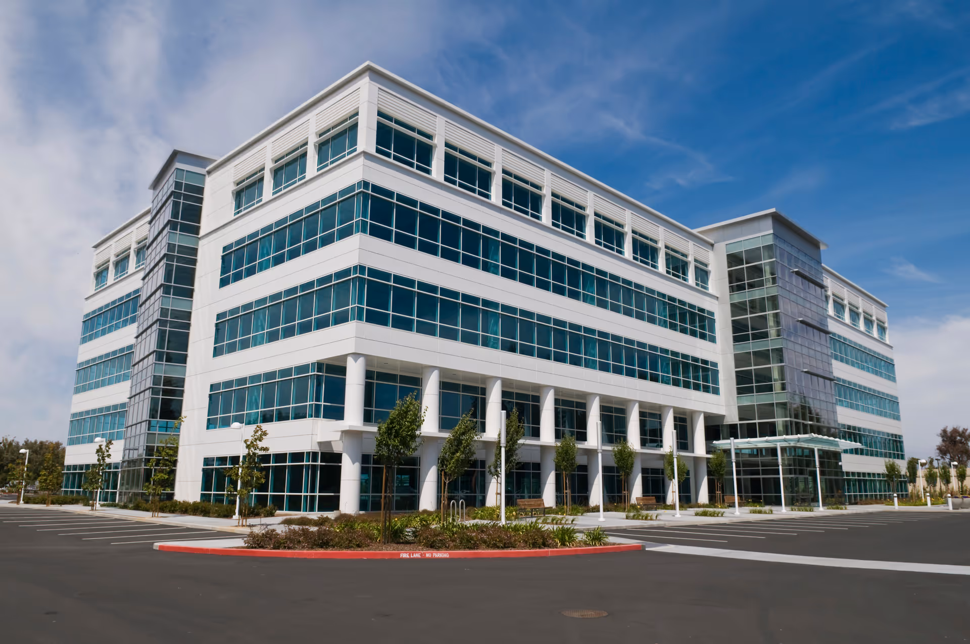 Modern multi-story senior living building with glass windows and a parking lot.