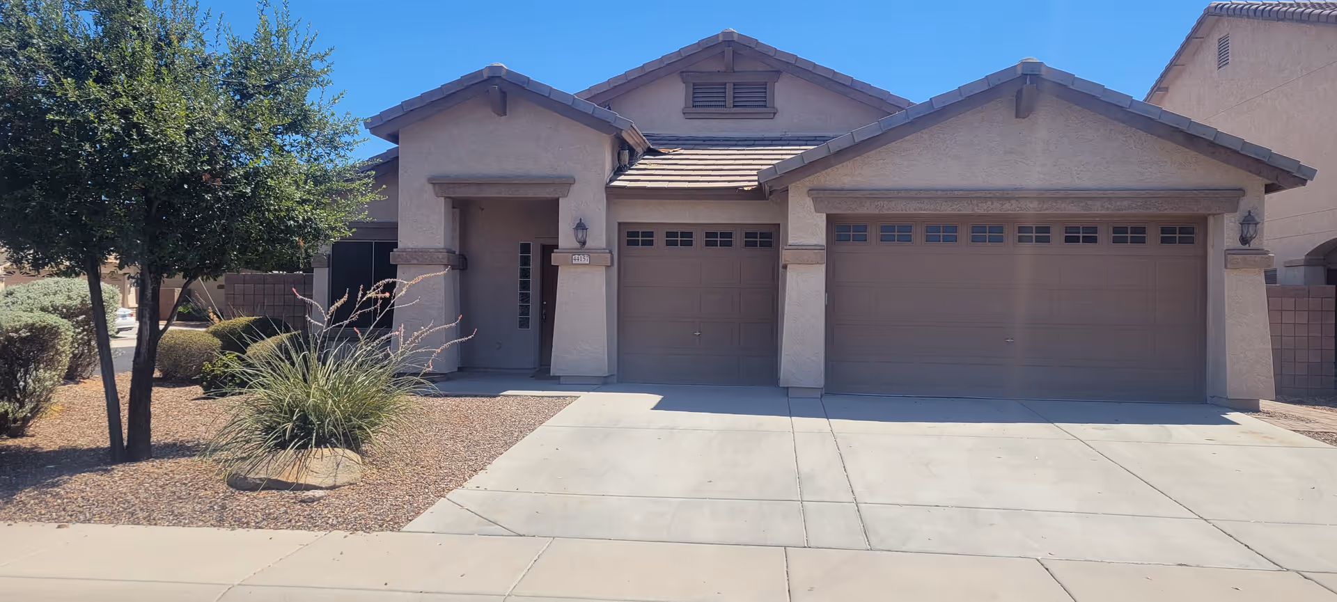 A single-story beige care home with a three-car garage and desert landscaping.