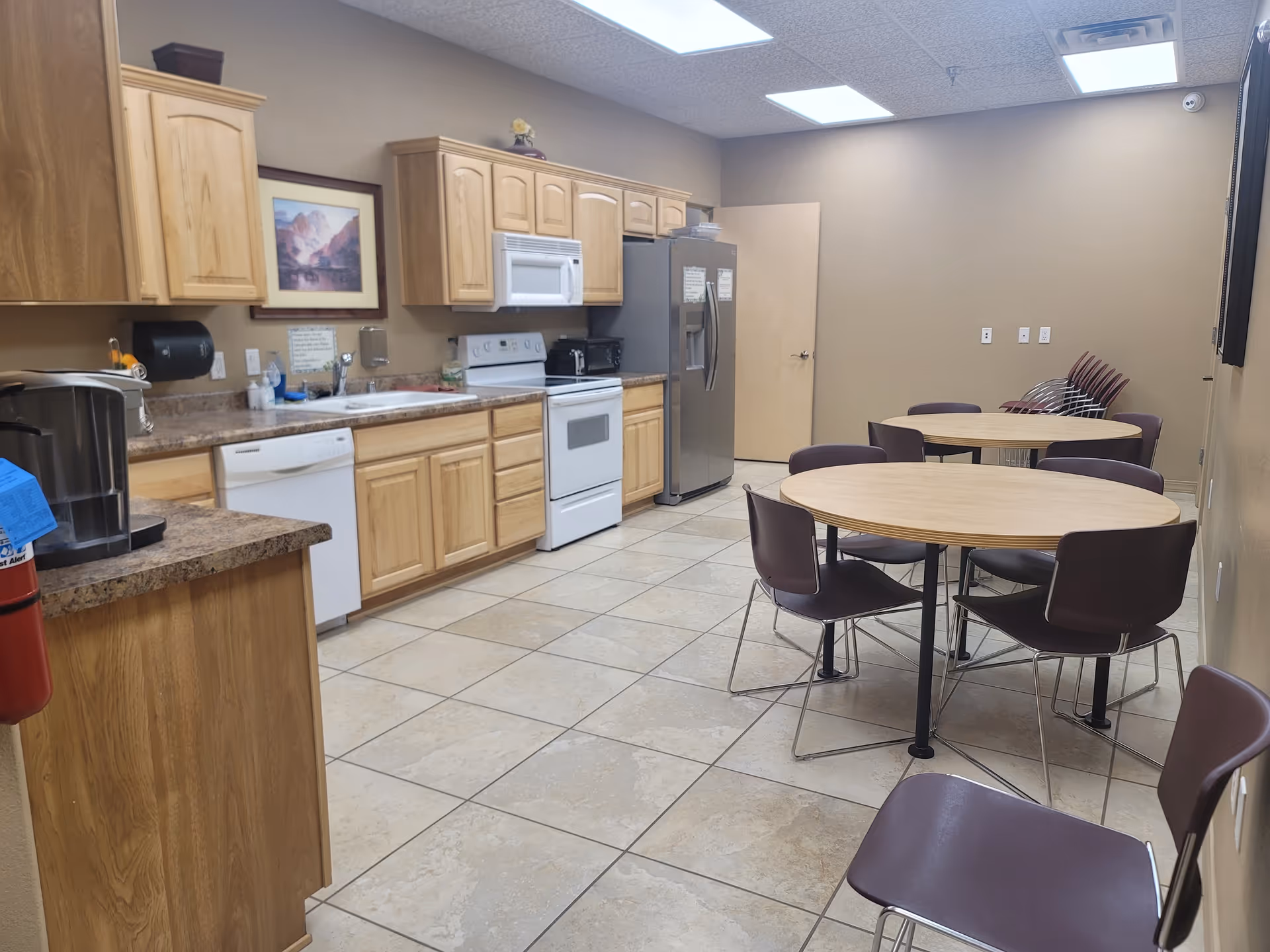 Interior kitchenette and dining area at Senior Wellness Homecare, with tables and brown chairs.