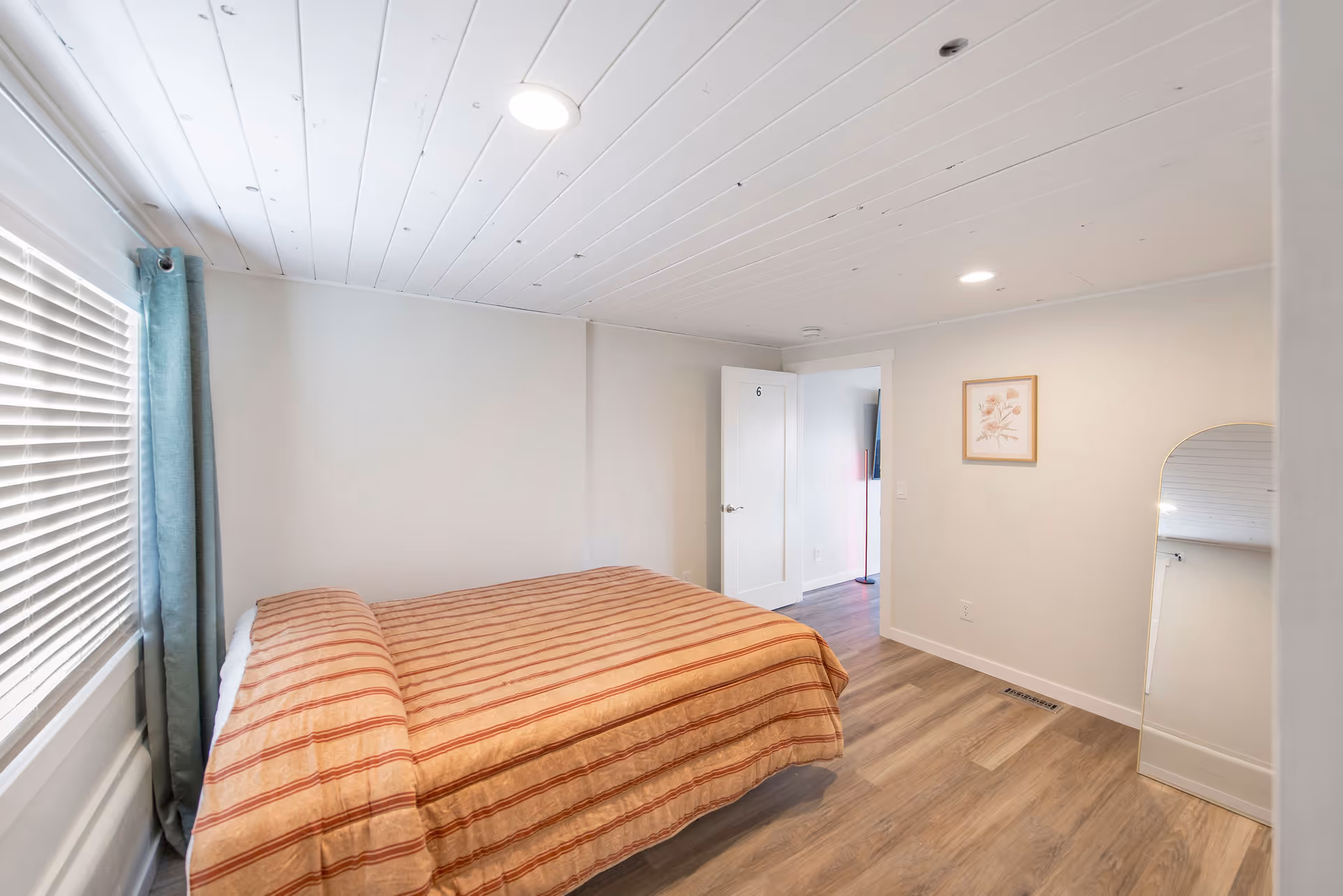 A simple bedroom with a striped comforter, window blinds, and a wall mirror.