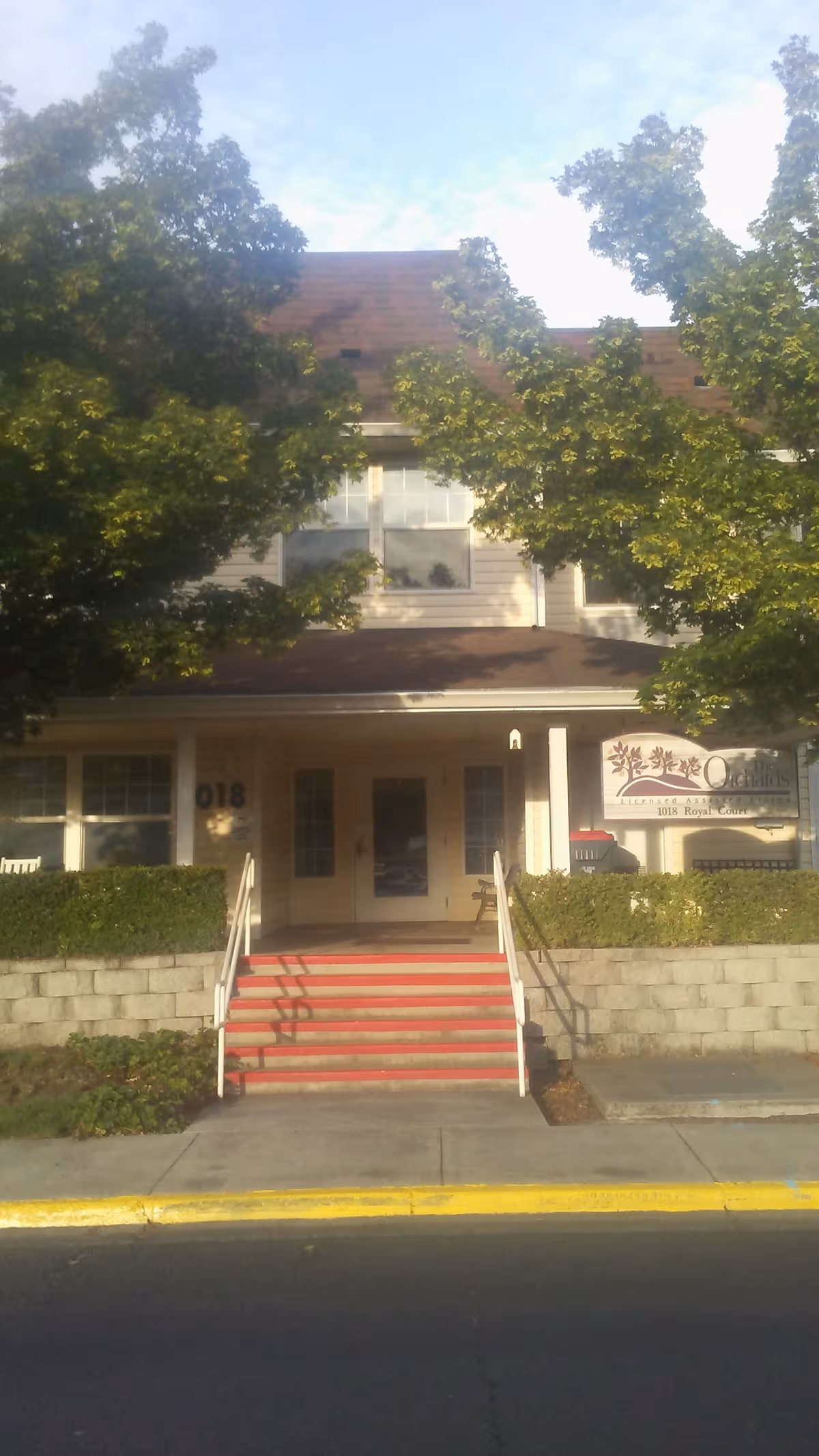 Front view of Orchards Assisted Living building with entrance stairs and sign.