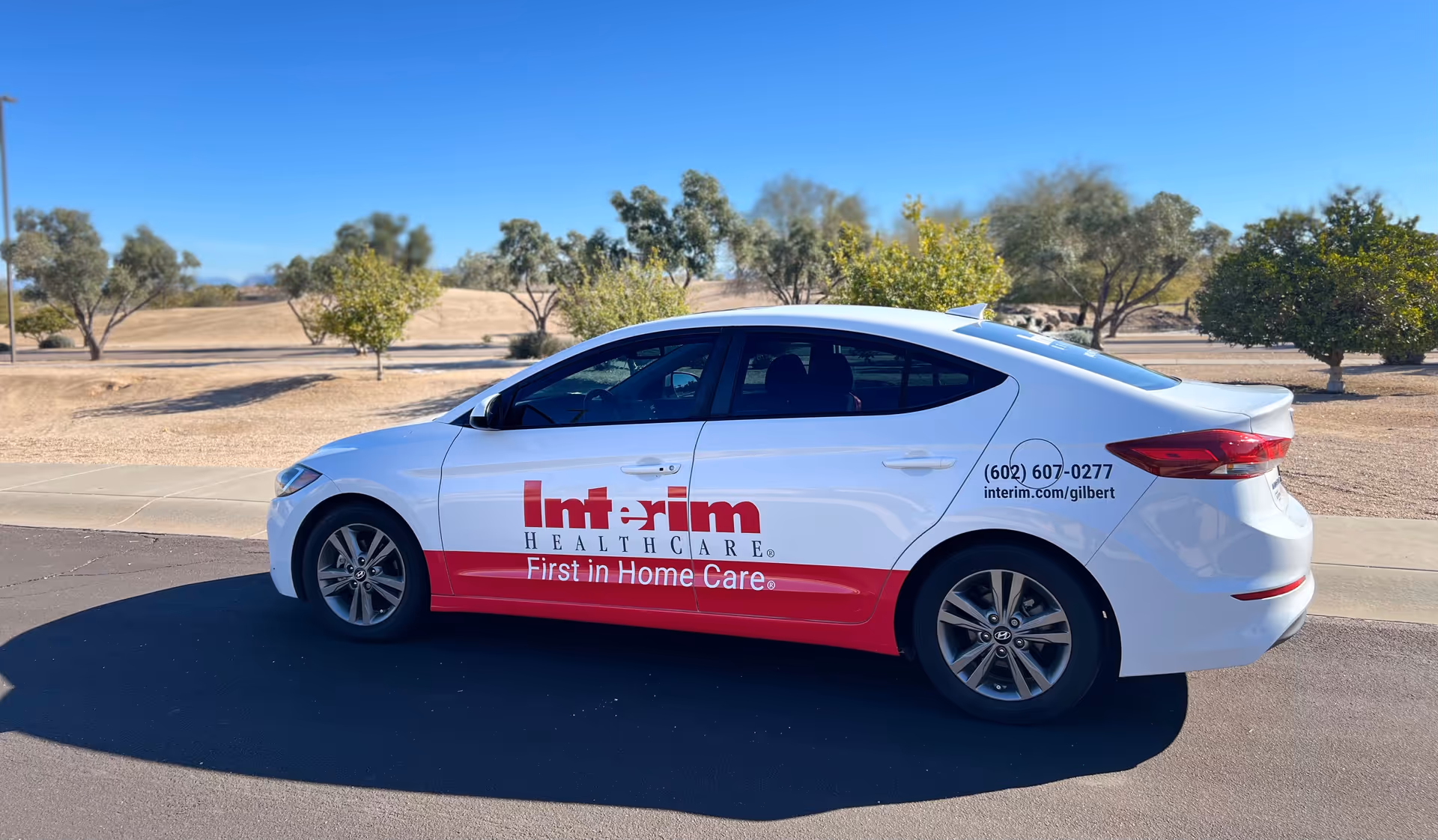 White Interim HealthCare Gilbert vehicle with red branding parked on a sunny street.
