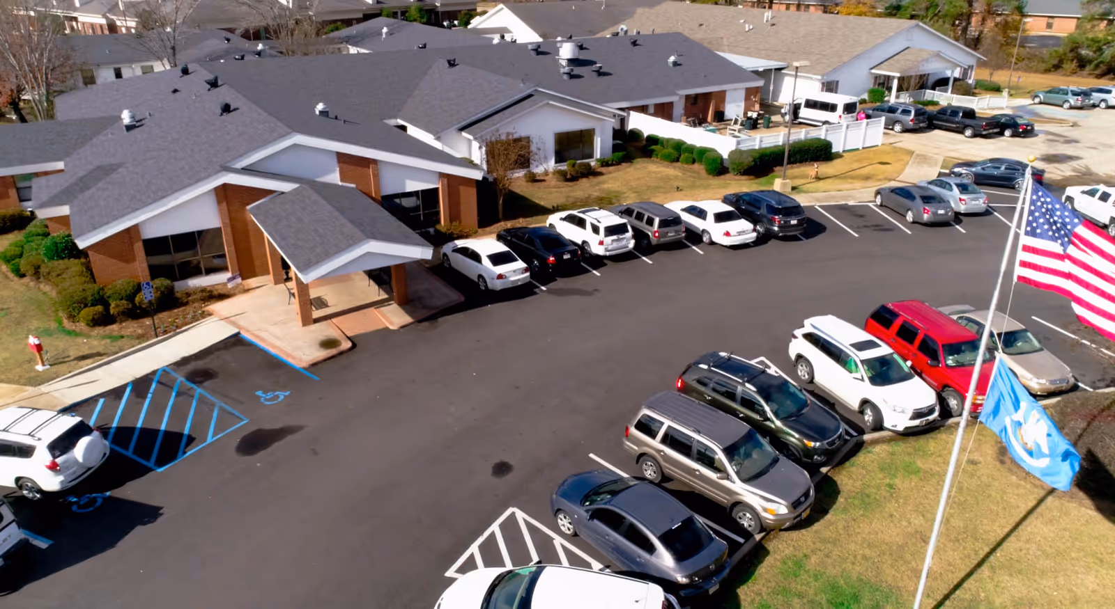 Aerial view of Avalon Place showing a single-story brick building, parking lot with multiple parked cars, and two flags.
