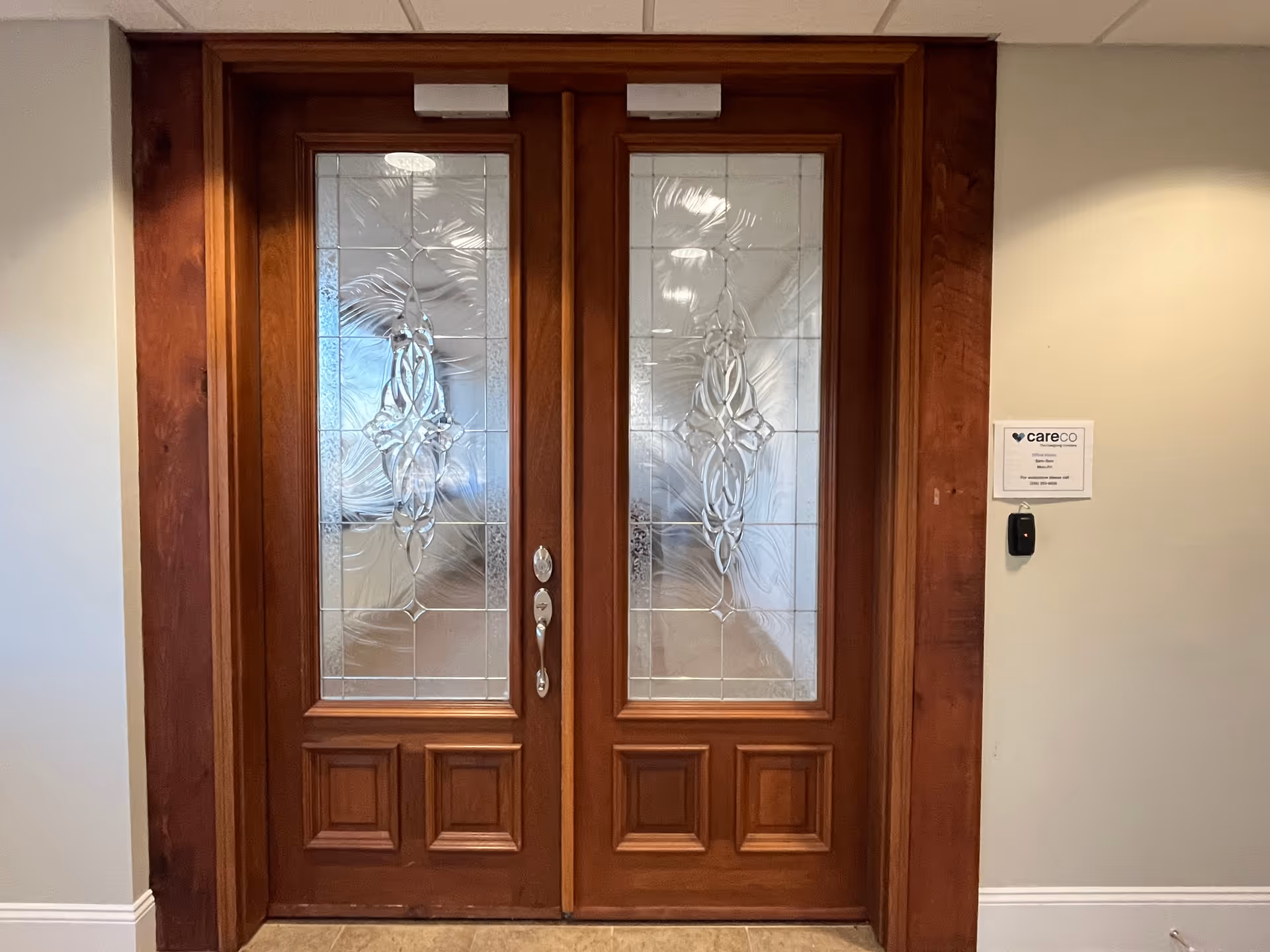 Double wooden doors with decorative glass panels in an interior hallway.