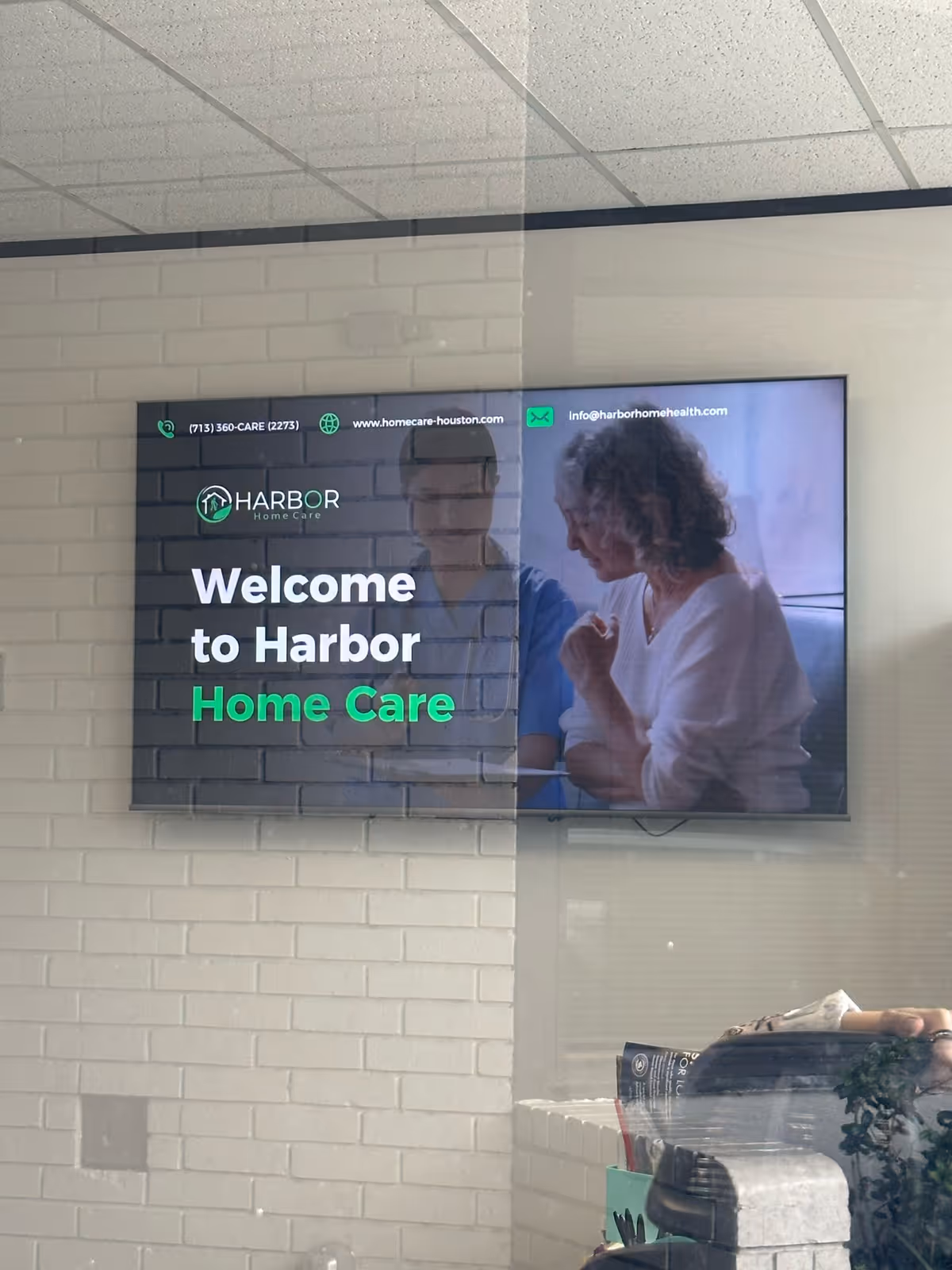 Wall-mounted digital display in an interior lobby shows Harbor Home Care welcome message.