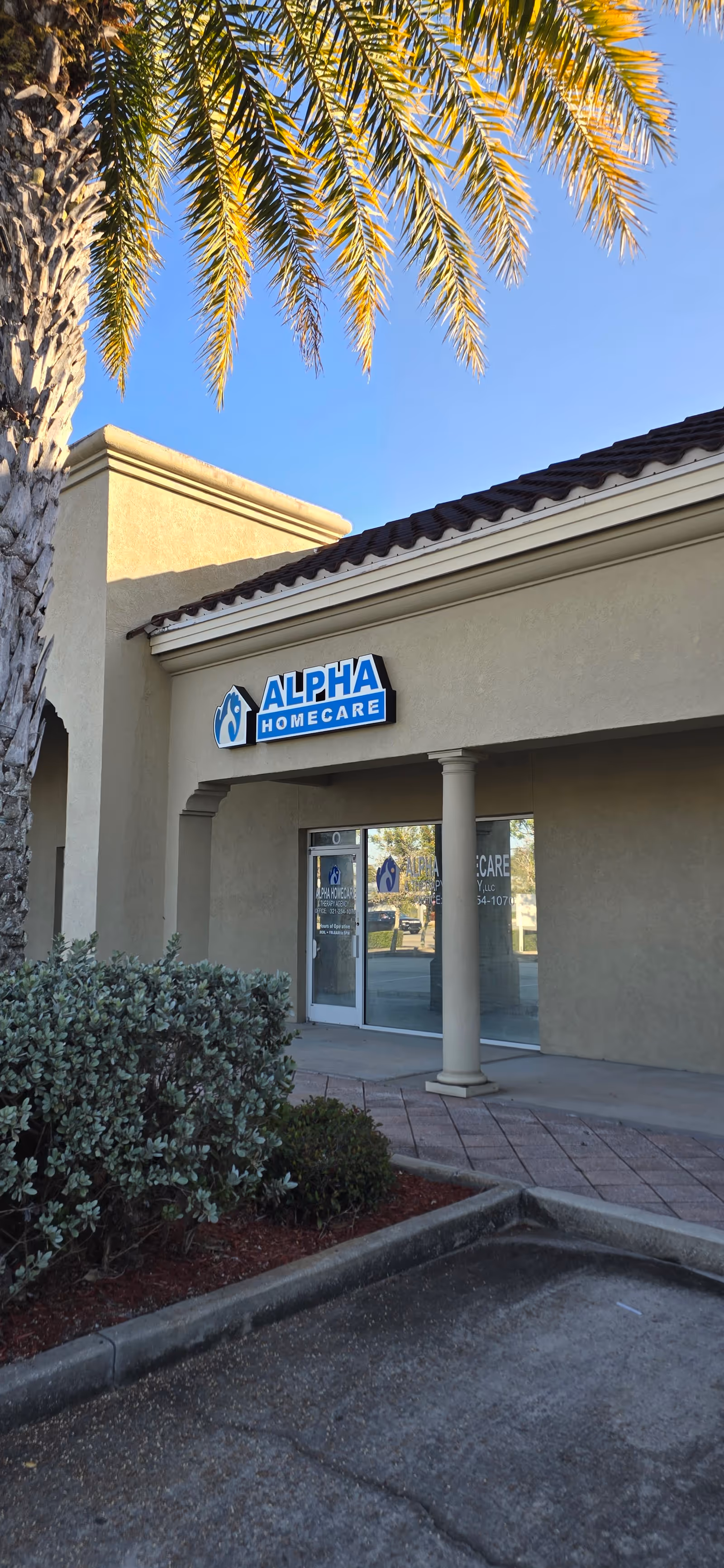 Front view of Alpha Home Care facility with porch, palm tree, and glass entrance.